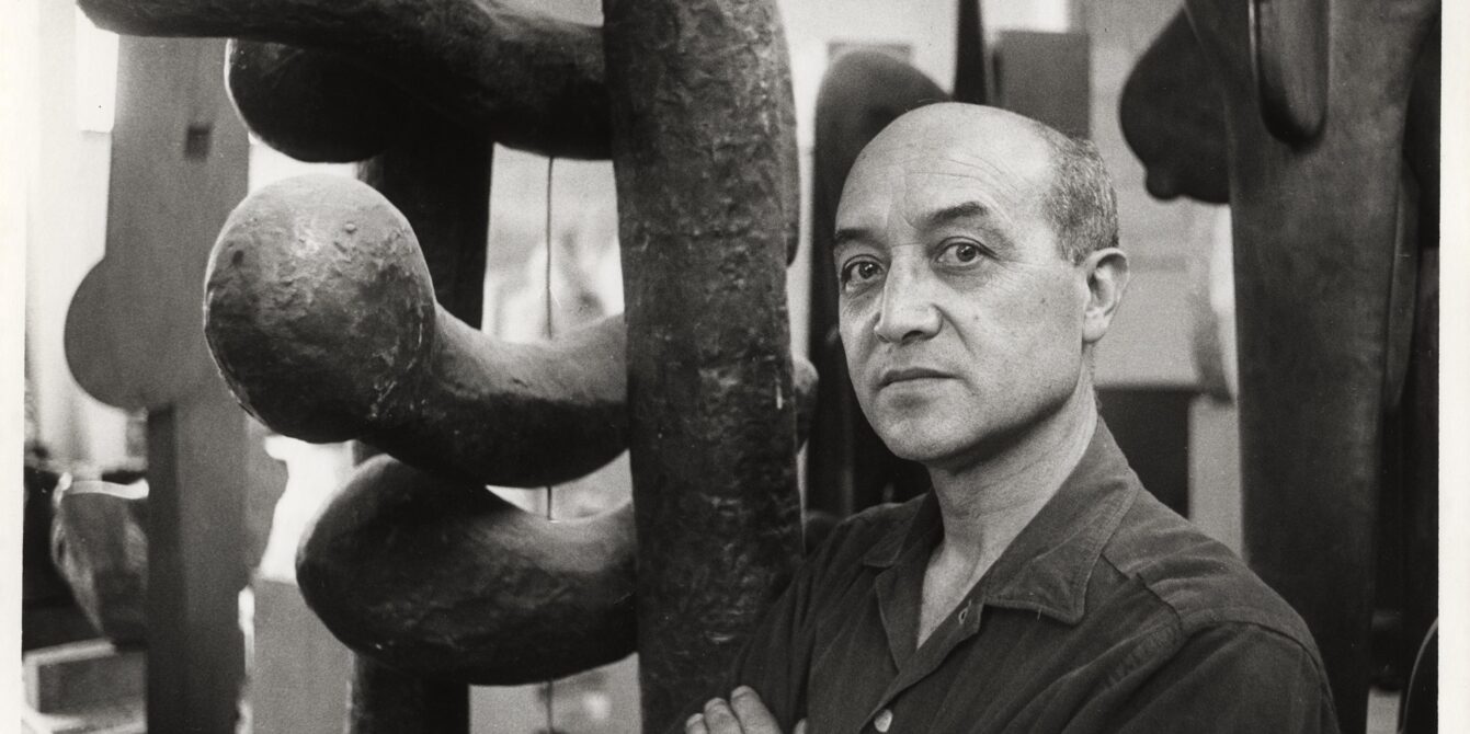 Portrait of artist and designer Isamu Noguchi standing next to one of his sculptures, The Isamu Noguchi Foundation and Garden Museum, New York