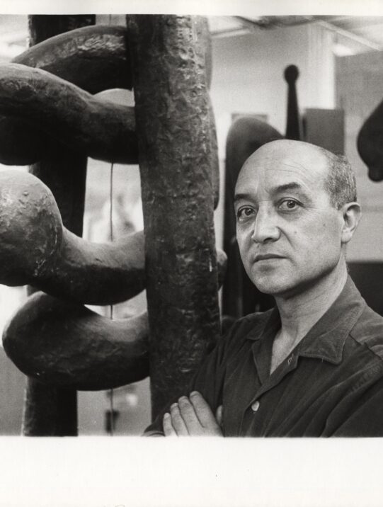 Portrait of artist and designer Isamu Noguchi standing next to one of his sculptures, The Isamu Noguchi Foundation and Garden Museum, New York