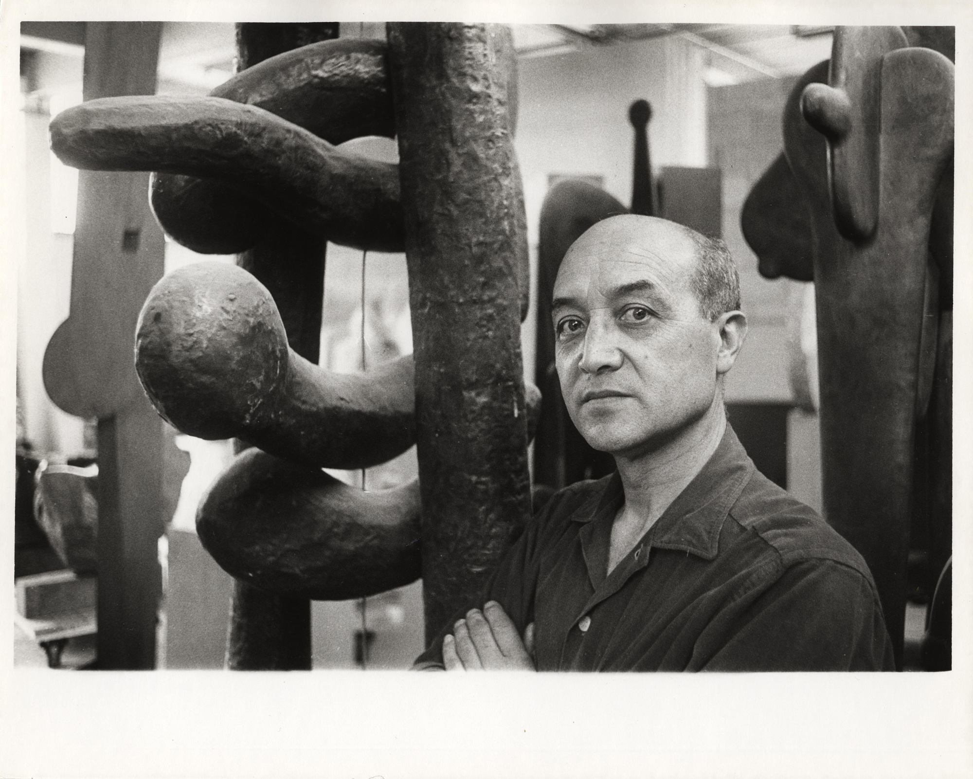Portrait of artist and designer Isamu Noguchi standing next to one of his sculptures