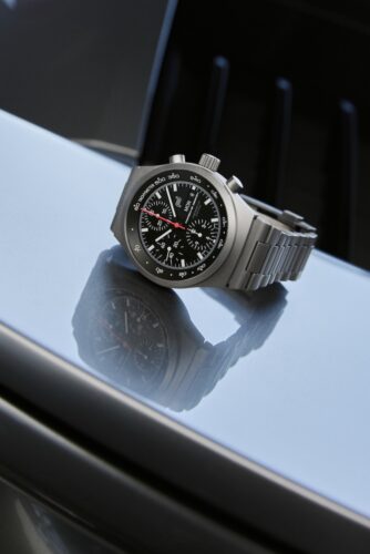 Porsche Design Chronograph 1 All Titanium mit schwarzem Zifferblatt und Titangehäuse auf einer spiegelnden Oberfläche.