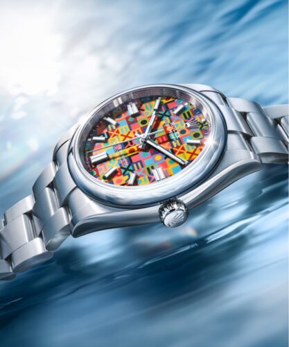 Rolex Oyster Jubiläumsmodell 2026 mit farbenfrohem grafischem Zifferblatt auf blau schimmernder Oberfläche.
