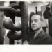 Portrait of artist and designer Isamu Noguchi standing next to one of his sculptures
